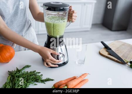 vue partielle de la femme préparant du smoothie frais près de la citrouille mûre et des carottes crues Banque D'Images