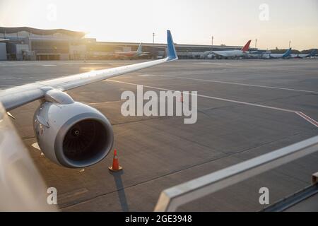 Gros plan d'une aile d'avion commercial près du terminal dans un aéroport au coucher du soleil Banque D'Images