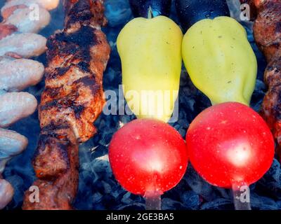 Les légumes crus et les morceaux de viande de différents degrés de préparation mis sur les brochettes sont frits sur le gril. Banque D'Images