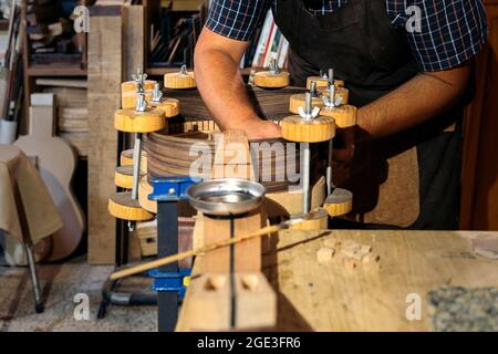 Artisan non reconnu créant une guitare et utilisant des outils dans un atelier traditionnel. Banque D'Images
