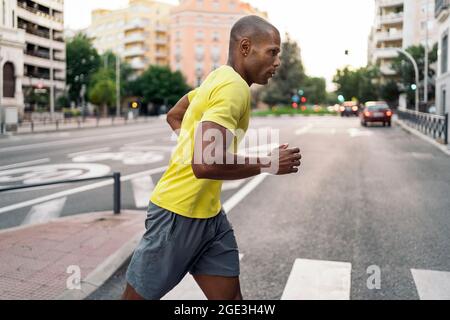 Vue latérale courte d'un athlète afro-américain avec un t-shirt jaune et un short de jogging sur les passages en ville en une journée ensoleillée. Banque D'Images