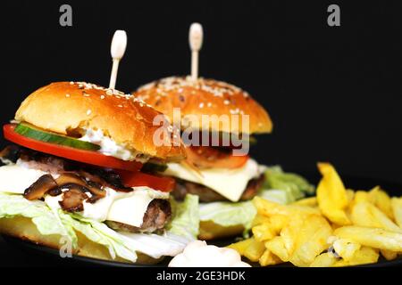 Hamburger et frites juteuses maison. Restauration rapide maison. Petits pains aux graines de sésame et garniture. Grand sandwich Banque D'Images