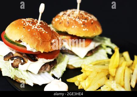 Hamburger et frites juteuses maison. Restauration rapide maison. Petits pains aux graines de sésame et garniture. Grand sandwich Banque D'Images