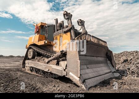 Excavatrice jaune dans les mouvements de carrière Les morts-terrains. Le sol, peignes de bulldozer avec le soleil clair et beau ciel bleu en arrière-plan Banque D'Images