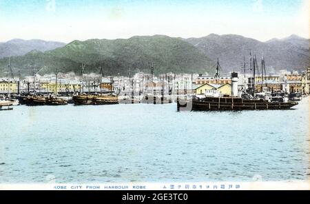 Ancienne carte postale japonaise de couleur main, vers 1910, du port de Kobe vu de la mer. Plusieurs bateaux de pêche japonais amarrés en premier plan. Banque D'Images