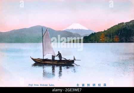 Vieille carte postale japonaise colorée à la main, vers 1910, petit bateau avec une seule voile traversant le lac Hakone avec le Mont Fuji en arrière-plan. Banque D'Images