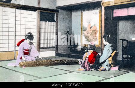 Ancienne carte postale japonaise de couleur main, vers 1910, d'une femme dans un kimono assise sur un sol tatami jouant un koto à une mère et un enfant aussi dans un kimono. Banque D'Images