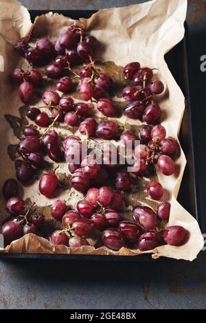 Raisins rouges avec épices et huile d'olive sur parchemin dans un plat à pâtisserie. Banque D'Images