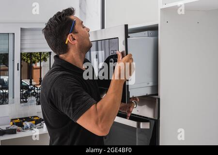 Homme plaçant un micro-ondes dans le trou d'un nouveau meuble de cuisine Banque D'Images