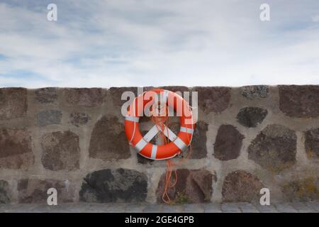 L'anneau de vie orange avec laisse est fixé au mur de brique devant le ciel bleu avec des nuages. Banque D'Images