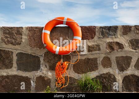 L'anneau de vie orange avec laisse est fixé au mur de brique devant le ciel bleu avec des nuages. Banque D'Images