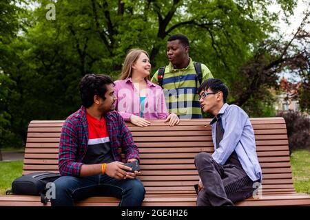 Joyeuse compagnie diversifiée d'amis d'université sur banc en bois Banque D'Images