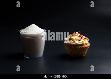 Cupcake et tasse de sucre gros plan, sur fond noir. Nourriture, qui contient une grande quantité de sucre, nocif pour la santé. Banque D'Images