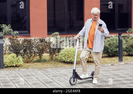 Portrait en longueur d'un homme contemporain senior à cheval dans la ville urbaine et utilisant un smartphone, espace de copie Banque D'Images