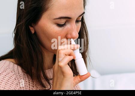 Une femme saupoudrer un médicament pour un froid d'un spray dans son nez Banque D'Images