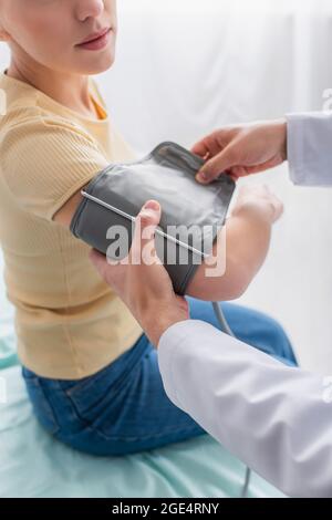 vue partielle du médecin mettant le brassard du tonomètre sur le bras du patient Banque D'Images