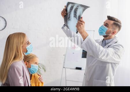 Pédiatre en masque médical regardant la fluorographie près de la mère et du patient Banque D'Images