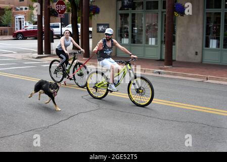 Un homme marche ou dirige son chien en laisse alors qu'il parcourt sa bicyclette dans une rue du centre-ville de Santa Fe, au Nouveau-Mexique. Banque D'Images