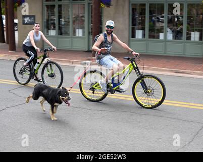 Un homme marche ou dirige son chien en laisse alors qu'il parcourt sa bicyclette dans une rue du centre-ville de Santa Fe, au Nouveau-Mexique. Banque D'Images