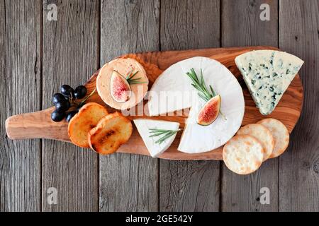 Plateau de fromages avec une sélection de fromages, crackers, figues et raisins sur un plateau de service en bois. Vue ci-dessus sur un fond de bois rustique. Banque D'Images