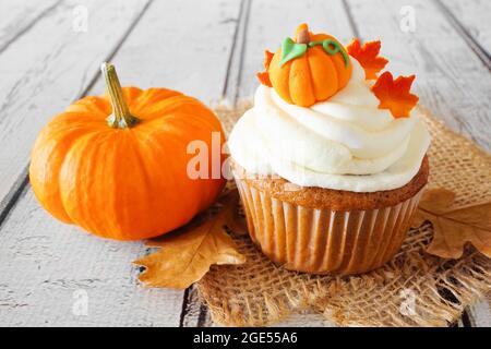 Petit gâteau aux épices à la citrouille d'automne avec glaçage crémeux et garnitures d'automne sur fond de bois blanc rustique Banque D'Images
