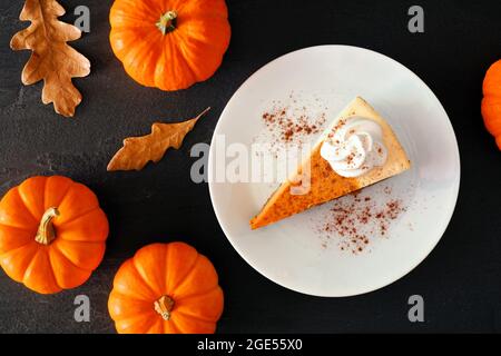 Tranche de cheesecake à la citrouille avec crème fouettée, scène de table au plafond avec un fond en pierre noire Banque D'Images