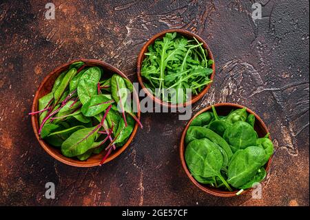 Mélanger les feuilles de salade, l'Arugula, les épinards et le Swiis Chard dans des bols en bois. Arrière-plan sombre. Vue de dessus Banque D'Images