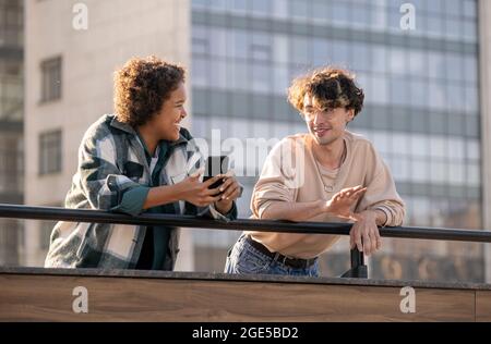 Deux adolescents contemporains discutent de quelque chose dans le smartphone d'une fille de race mixte dans un environnement urbain Banque D'Images