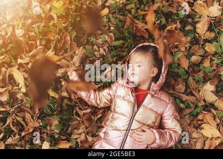 Petite fille blonde joue avec des feuilles d'automne jaunes dans le jardin, sourire, a du plaisir Banque D'Images