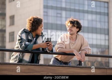 Deux adolescents multiraciaux qui interagissent en milieu urbain tandis que l'un d'eux utilise un smartphone Banque D'Images