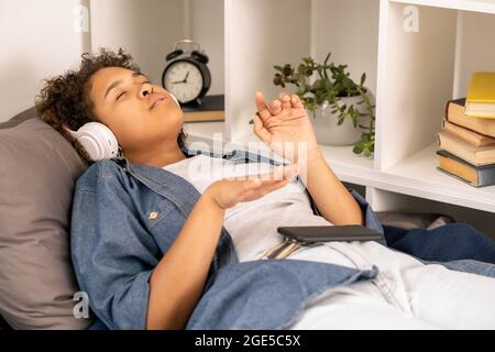 Adolescente contemporaine avec un casque qui écoute sa musique préférée sur son lit Banque D'Images