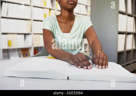 Gros plan d'une femme afro-américaine méconnaissable lisant un livre en braille dans une bibliothèque universitaire, un espace de copie Banque D'Images