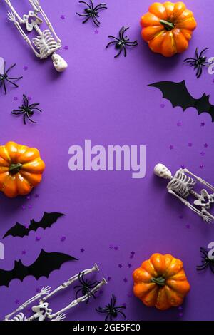 Bonne maquette de l'affiche d'Halloween. Citrouilles plates, squelettes effrayants, silhouettes de chauve-souris sur fond violet. Vue de dessus, au-dessus de la tête. Banque D'Images