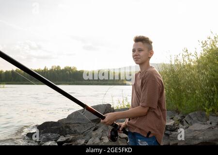 Adolescent contemporain avec pêche à la perche seule au bord du lac le week-end d'été Banque D'Images