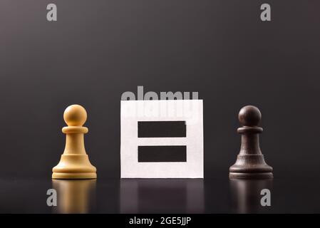 Concept d'égalité entre les personnes avec des pièces d'échecs noir et blanc avec fond sombre et écriteau avec signe égal Banque D'Images