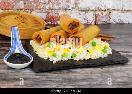 Rouleaux de printemps remplis de légumes et de canard croustillant chinois avec riz aux œufs sur un plateau de service en ardoise Banque D'Images