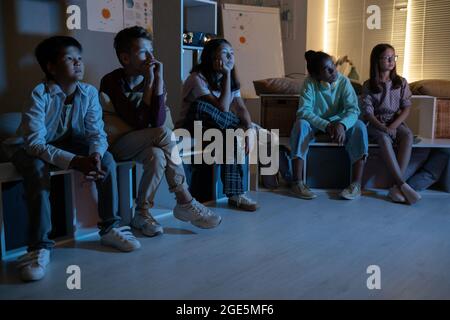 Groupe d'enfants regardant un film ou autre chose en étant assis sur des bancs dans l'obscurité Banque D'Images