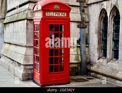 Phone Box - téléphone emblématique de Londres dans le rouge vif se tenant contre un bâtiment de style classique avec des fenêtres voûtées et des pierres traditionnelles. Banque D'Images