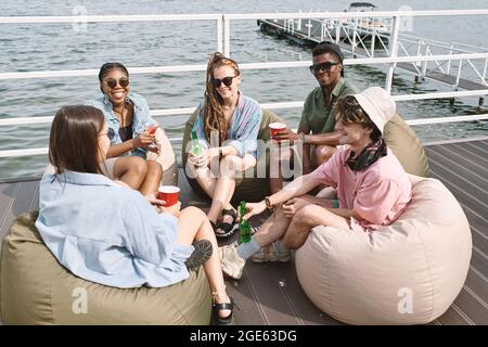 Divers groupes d'amis appréciant passer du temps ensemble, assis sur la jetée, boire et parler Banque D'Images