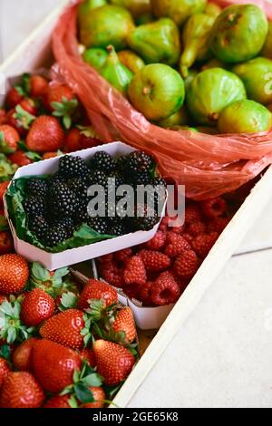 Un coffret en bois avec des boîtes de fraises, framboises, figues et mûres se trouve sur une tuile Banque D'Images