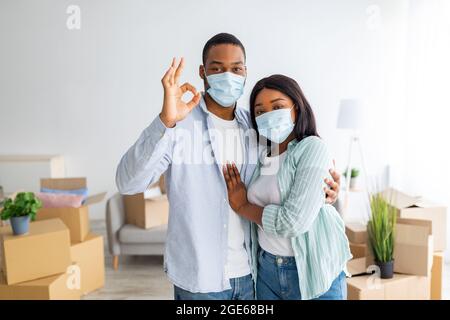 Portrait d'un couple afro-américain aimant dans des masques montrant des clés, debout dans sa propre maison pleine de boîtes en carton avec des effets personnels. Acheteurs immobiliers, maison Banque D'Images