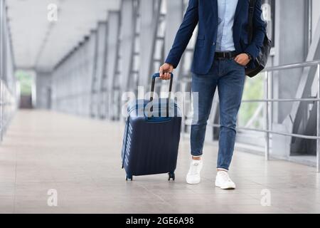 Homme méconnaissable en vêtements décontractés marchant avec des bagages au terminal de l'aéroport, voyageur masculin se rendant à la porte d'embarquement avec Suitcase, prêt pour les affaires Banque D'Images