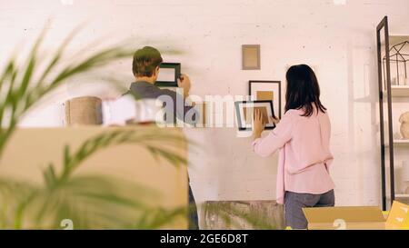 vue arrière de deux cadres photo suspendus sur le mur près des boîtes dans la nouvelle maison, image de stock Banque D'Images