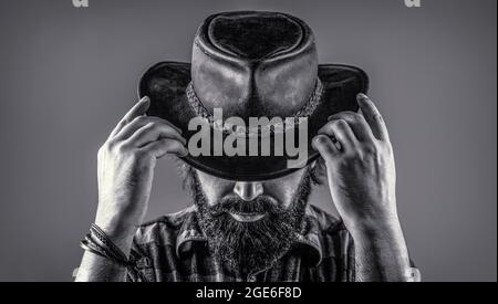 Cow-boys non rasés. Cow-boy américain. Chapeau de cowboy en cuir. Portrait d'un jeune homme portant un chapeau de cow-boy. Cowboys en chapeau. Jolie macho barbu. Noir et Banque D'Images