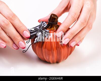 Mains de femmes avec une manucure française d'automne tendance avec des bouts rouges au bord libre de l'ongle. Citrouille décorative en céramique sur fond blanc. Orange s Banque D'Images