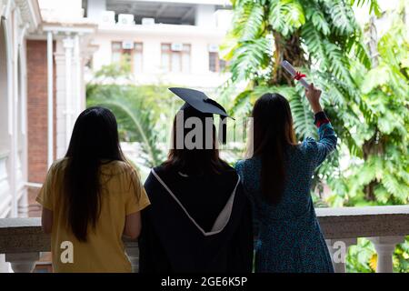 Joyeux et joyeux les étudiantes et étudiants diplômés de l'université en robe universitaire bavarder avec des amis qui sont venus pour féliciter le jour de la congrégation Banque D'Images