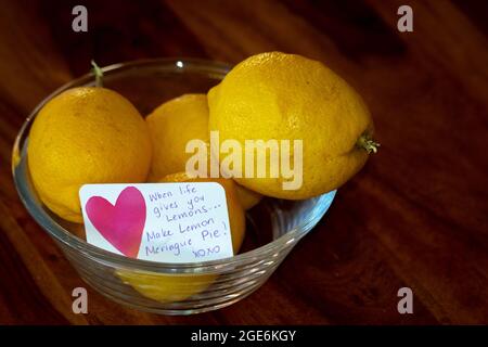 Citrons jaunes dans un bol en verre avec note, quand la vie vous donne des citrons... faites de la tarte au citron meringue! Banque D'Images