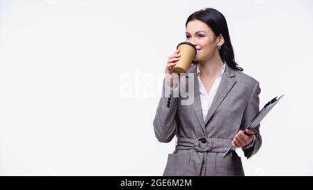 Femme d'affaires en veste buvant du café à emporter et tenant le presse-papiers isolé sur blanc Banque D'Images