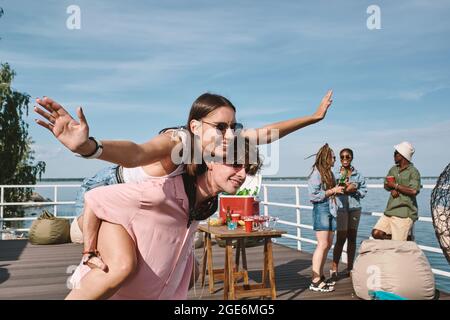 Beau jeune homme attrayant donnant le pigeyback à la jolie jeune femme à la fête en plein air Banque D'Images