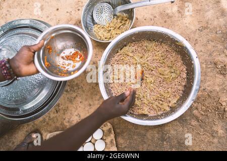 Gros plan au-dessus de la vue d'un plat africain noir non reconnaissable assaisonnement d'une grande assiette de céréales avec des oignons, du paprika et des tomates Banque D'Images